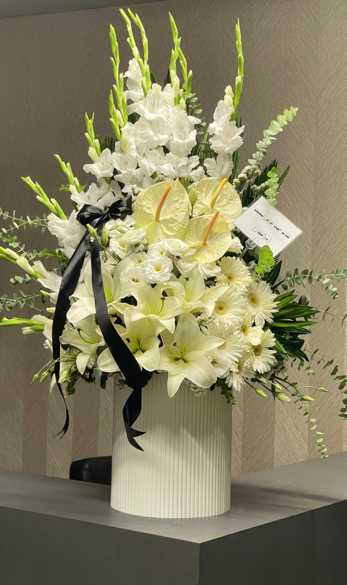 <h2>باکس گل ترحیم لاکچری سفید</h2> <p>این آرایش گل سفارشی، با الهام از زیبایی و وقار گل‌های سفید، انتخابی ایده‌آل برای ابراز همدردی و احترام در مراسم ترحیم است. ترکیب گل‌های شمشیری بلند، لیلیوم معطر، آنتریم و داوودی در کنار روبان مشکی ساتن، ظاهری لوکس و در عین حال متین به این باکس بخشیده است.</p> <ul> <li><strong>ترکیب گل‌ها:</strong> گل شمشیری سفید، لیلیوم، آنتریم و داوودی</li> <li><strong>طراحی:</strong> گلدان سفارشی سفید با خطوط عمودی و روبان مشکی</li> <li><strong>مناسب برای:</strong> پیام تسلیت، مراسم ختم و ترحیم</li> <li><strong>ویژگی‌ها:</strong> گل‌های تازه و طبیعی، طراحی مدرن و شیک</li> </ul> <p>این باکس گل، پیام تسلیت شما را با شکوه و وقار به بازماندگان منتقل می‌کند.</p>