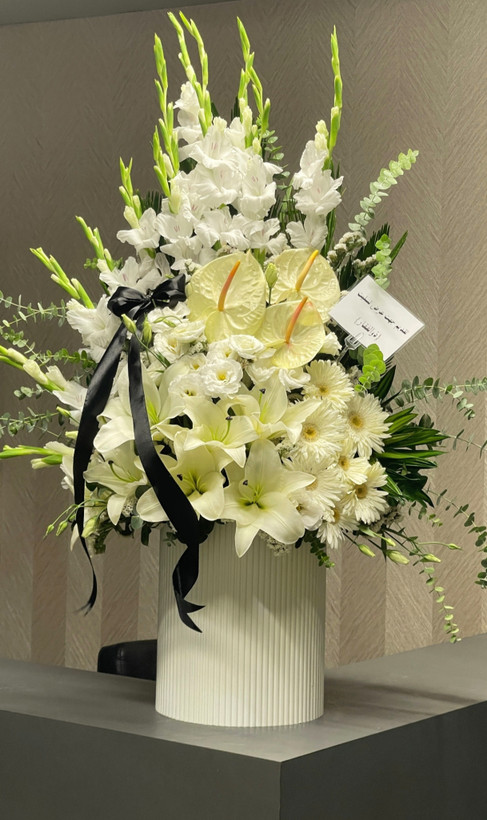 <h2>باکس گل ترحیم لاکچری سفید</h2> <p>این آرایش گل سفارشی، با الهام از زیبایی و وقار گلهای سفید، انتخابی ایدهآل برای ابراز همدردی و احترام در مراسم ترحیم است. ترکیب گلهای شمشیری بلند، لیلیوم معطر، آنتریم و داوودی در کنار روبان مشکی ساتن، ظاهری لوکس و در عین حال متین به این باکس بخشیده است.</p> <ul> <li><strong>ترکیب گلها:</strong> گل شمشیری سفید، لیلیوم، آنتریم و داوودی</li> <li><strong>طراحی:</strong> گلدان سفارشی سفید با خطوط عمودی و روبان مشکی</li> <li><strong>مناسب برای:</strong> پیام تسلیت، مراسم ختم و ترحیم</li> <li><strong>ویژگیها:</strong> گلهای تازه و طبیعی، طراحی مدرن و شیک</li> </ul> <p>این باکس گل، پیام تسلیت شما را با شکوه و وقار به بازماندگان منتقل میکند.</p>